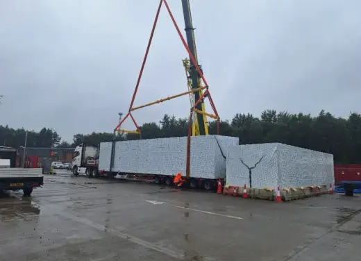 Lorry-mounted crane lifting a long modular unit in a yard