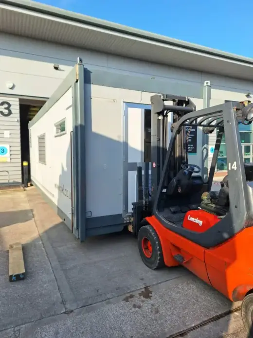 Red forklift moving a portable cabin into an industrial unit