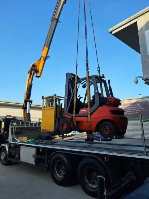 HIAB crane lifting a red forklift onto a flatbed lorry