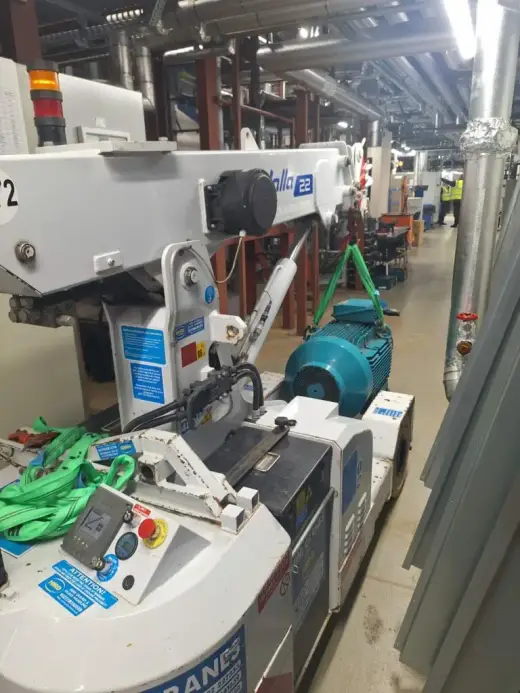 Compact crane lifting an electric motor in a plant room corridor