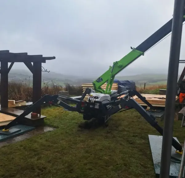Green spider crane lifting a timber frame in a garden