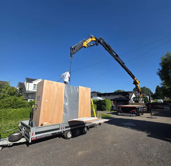 HIAB crane lifting a wooden crate beside a house