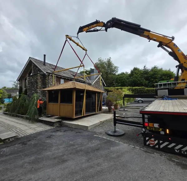 HIAB crane lifting a timber building beside a house