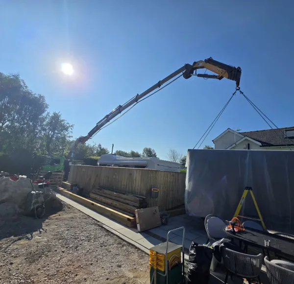 HIAB crane lifting a garden building panel over a fence