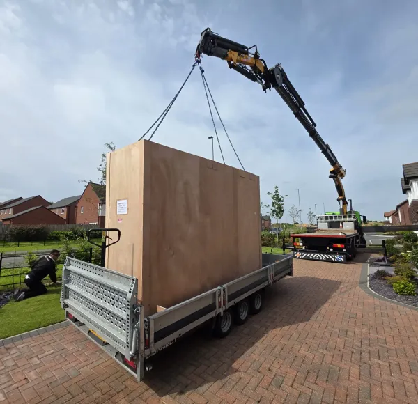 HIAB crane lifting a large crate from a trailer on a driveway