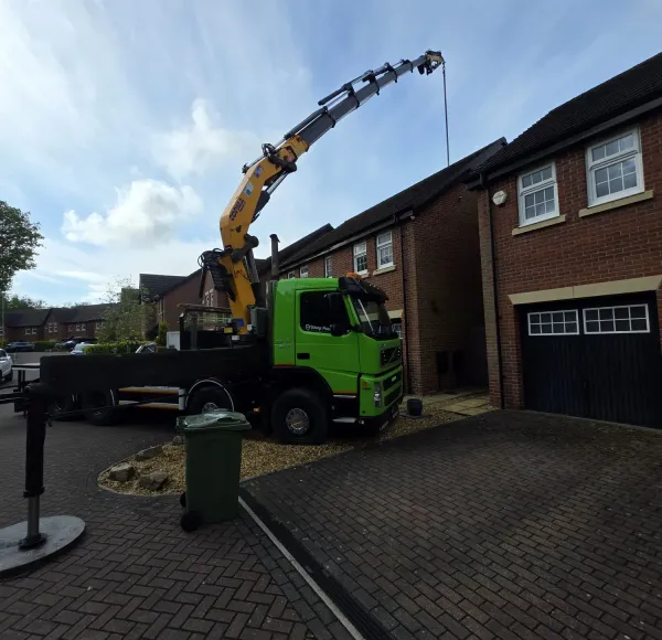 Green HIAB lorry with its crane raised beside a new-build home