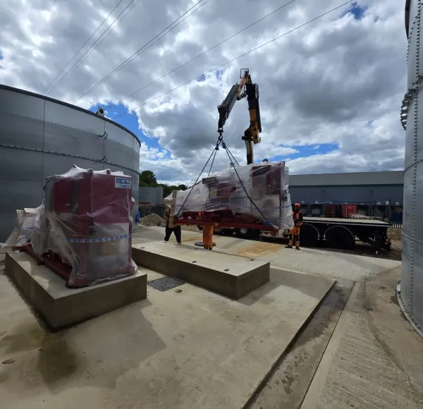 Wrapped machinery lowered onto a concrete plinth beside storage tanks