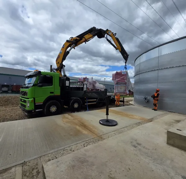 Operatives guiding machinery lifted by a HIAB lorry beside a tank