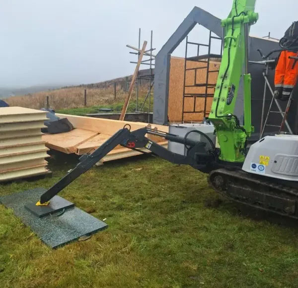 Green spider crane lifting timber at a new-build house