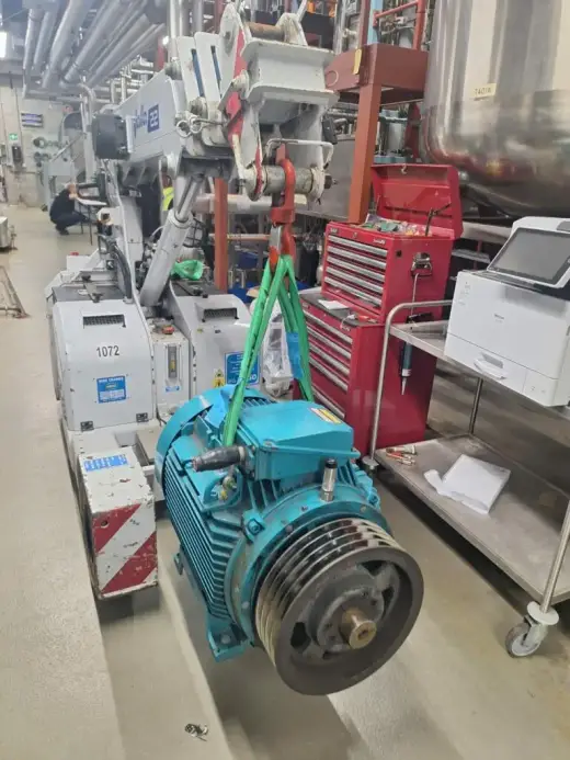 Electric motor lifted by crane inside a workshop