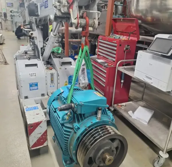 Electric motor lifted by crane inside a workshop