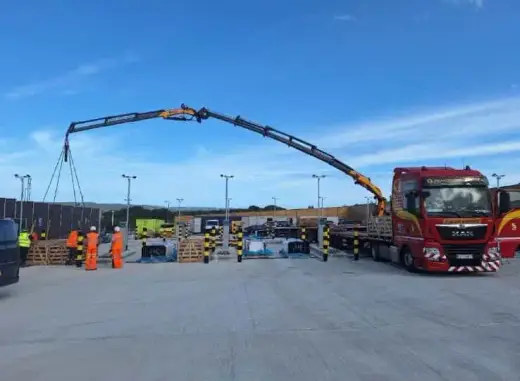 Lorry-mounted crane with its boom extended over a car park
