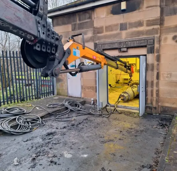 Crane lifting machinery out of a brick building doorway