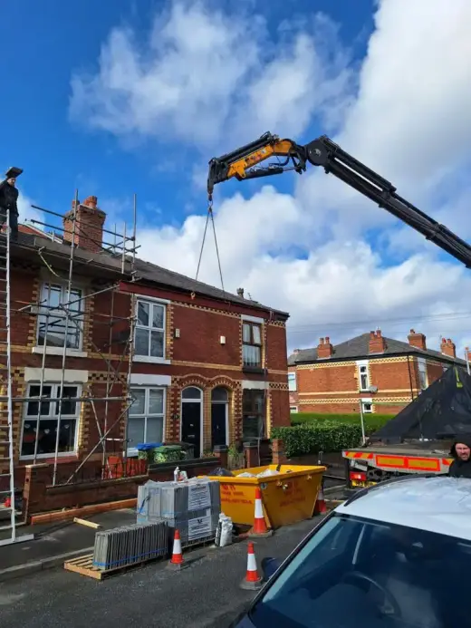 HIAB crane lifting at terraced houses beside a skip