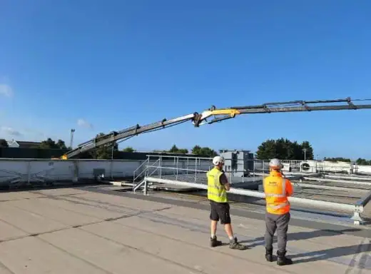 Operatives watching a long HIAB boom extend across a rooftop
