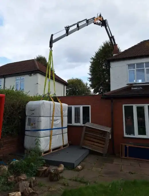 HIAB crane lifting a hot tub into a garden beside a house