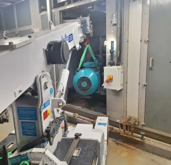 Compact crane lifting an electric motor inside a plant room