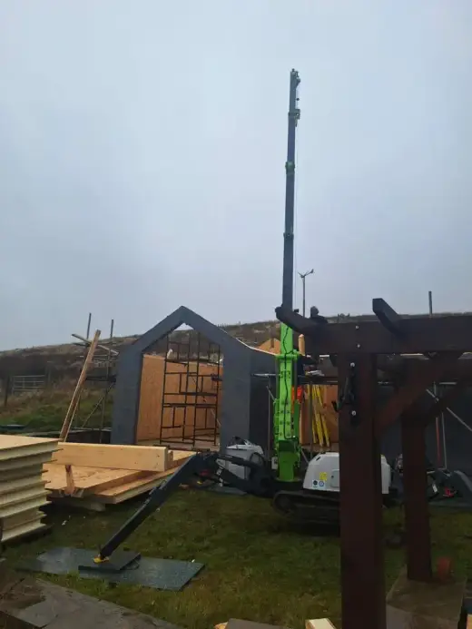 Spider crane beside a timber cabin on a hillside site