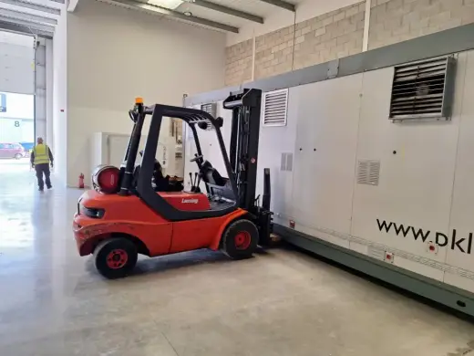 Red forklift moving a large portable cabin inside a unit
