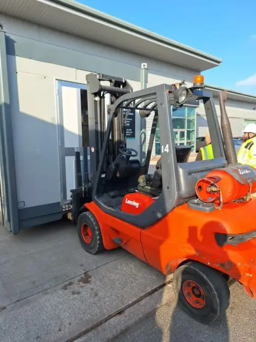 Orange forklift moving a portable cabin outdoors