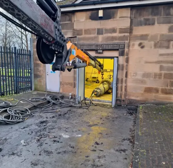 Crane lifting machinery out through a building doorway